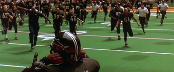 Movie still from “Any Given Sunday” (1999), directed by Oliver Stone – A group of football players running on a field; Extreme Wide shot, High angle