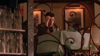 Movie still from “Anything Else” (2003), directed by Woody Allen – A man sitting at a table with a glass of wine in front of him; Medium shot, Over the shoulder angle