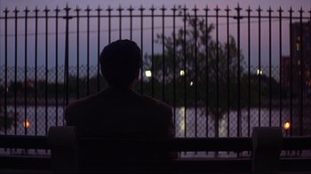 Movie still from “Anything Else” (2003), directed by Woody Allen – A man sitting on top of a bench looking out a fence; Wide shot, Over the shoulder angle