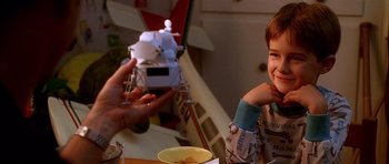 Movie still from “Apollo 13” (1995), directed by Ron Howard – A person taking a picture of a child with a toy airplane; Close Up shot, Over the shoulder angle