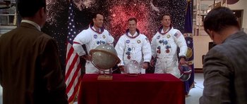Movie still from “Apollo 13” (1995), directed by Ron Howard – Three men in space suits standing in front of a table; Wide shot, Overhead angle
