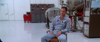 Movie still from “Apollo 13” (1995), directed by Ron Howard – A man sitting in a chair in front of a machine; Medium shot, Over the shoulder angle
