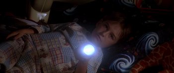 Movie still from “Apollo 13” (1995), directed by Ron Howard – A boy laying in bed holding a flashlight; Medium shot, High angle