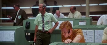 Movie still from “Apollo 13” (1995), directed by Ron Howard – A man with a tie and a headset on in front of other men; Medium shot, Low angle