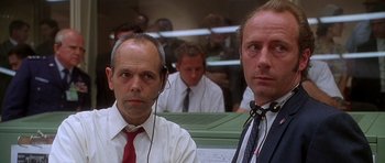Movie still from “Apollo 13” (1995), directed by Ron Howard – Two men in suits and ties sitting next to each other in front of other men; Close Up shot, Low angle