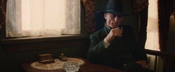 Movie still from “Appaloosa” (2008), directed by Ed Harris – A man sitting at a table with a cigarette in his mouth; Medium shot, Low angle