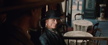 Movie still from “Appaloosa” (2008), directed by Ed Harris – A man wearing a black hat sitting at a table in a room; Close Up shot, Over the shoulder angle
