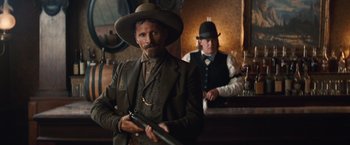Movie still from “Appaloosa” (2008), directed by Ed Harris – A man holding a rifle in a room; Medium shot, Low angle