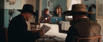 Movie still from “Appaloosa” (2008), directed by Ed Harris – A woman sitting at a table drinking a cup of coffee; Medium shot, Over the shoulder angle