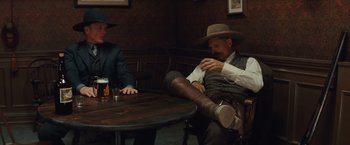 Movie still from “Appaloosa” (2008), directed by Ed Harris – Two men sitting at a table with a beer in front of them; Medium shot, Over the shoulder angle