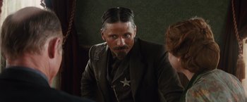 Movie still from “Appaloosa” (2008), directed by Ed Harris – A man with a long beard and a star on his suit jacket; Close Up shot, Over the shoulder angle