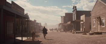 Movie still from “Appaloosa” (2008), directed by Ed Harris – People are walking down a dirt road in the middle of a western town; Extreme Wide shot, Low angle