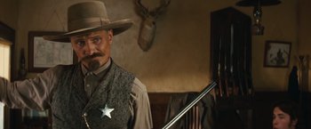 Movie still from “Appaloosa” (2008), directed by Ed Harris – A man in a cowboy hat holding a rifle; Medium shot, Low angle