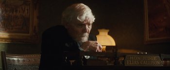 Movie still from “Appaloosa” (2008), directed by Ed Harris – An older man sitting at a desk in a dark room; Medium shot, Over the shoulder angle