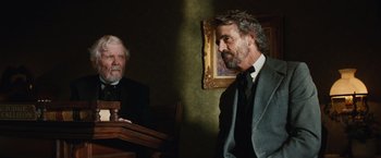 Movie still from “Appaloosa” (2008), directed by Ed Harris – Two men in suits and ties are standing in front of a judge's bench; Medium shot, Over the shoulder angle