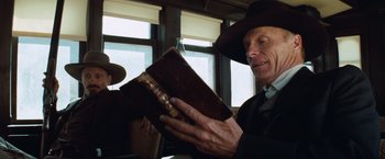 Movie still from “Appaloosa” (2008), directed by Ed Harris – An old man wearing a cowboy hat holding an old book; Close Up shot, Low angle