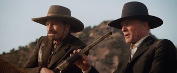 Movie still from “Appaloosa” (2008), directed by Ed Harris – A man holding a rifle and another man wearing a hat; Close Up shot, Low angle