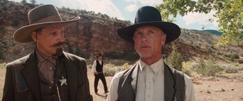 Movie still from “Appaloosa” (2008), directed by Ed Harris – A man wearing a hat and a vest standing next to another man in a hat; Medium shot, Low angle