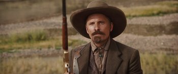 Movie still from “Appaloosa” (2008), directed by Ed Harris – A man with a beard and a hat holding a rifle; Close Up shot, Over the shoulder angle