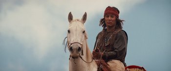 Movie still from “Appaloosa” (2008), directed by Ed Harris – A man in native american garb sitting on a white horse; Medium shot, Low angle
