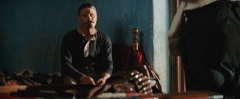 Movie still from “Appaloosa” (2008), directed by Ed Harris – A man sitting on a couch in front of a wall; Medium shot, Over the shoulder angle