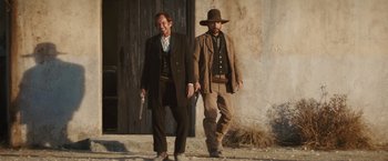 Movie still from “Appaloosa” (2008), directed by Ed Harris – A couple of men walking down a street holding guns; Medium shot, Low angle