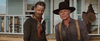 Movie still from “Appaloosa” (2008), directed by Ed Harris – Two men standing next to each other in front of a house; Medium shot, Low angle