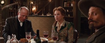 Movie still from “Appaloosa” (2008), directed by Ed Harris – A woman sitting at a table with a glass of red wine; Medium shot, Over the shoulder angle