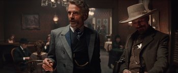 Movie still from “Appaloosa” (2008), directed by Ed Harris – A man wearing a suit and tie in a room; Medium shot, Over the shoulder angle