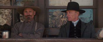 Movie still from “Appaloosa” (2008), directed by Ed Harris – Two men sitting next to each other in front of a painting; Medium shot, Low angle