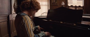 Movie still from “Appaloosa” (2008), directed by Ed Harris – A woman sitting at a piano playing a song; Medium shot, High angle