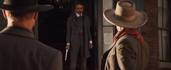 Movie still from “Appaloosa” (2008), directed by Ed Harris – A man holding a gun while standing in front of a building; Medium shot, Over the shoulder angle