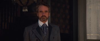 Movie still from “Appaloosa” (2008), directed by Ed Harris – A man wearing a suit and tie standing in front of a wall; Close Up shot, Over the shoulder angle