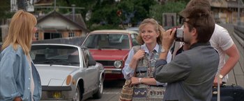 Movie still from “April Fool's Day” (1986), directed by Fred Walton – A man taking a picture of a woman with a purse; Medium shot, Over the shoulder angle