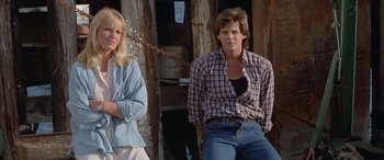 Movie still from “April Fool's Day” (1986), directed by Fred Walton – A man and a woman standing next to each other in front of a wooden structure; Medium shot, Low angle