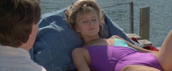 Movie still from “April Fool's Day” (1986), directed by Fred Walton – A beautiful young lady laying on top of a bed next to the ocean; Medium shot, High angle