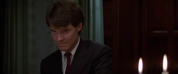 Movie still from “April Fool's Day” (1986), directed by Fred Walton – A man in a suit and tie sitting in front of a window; Close Up shot, Low angle