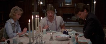 Movie still from “April Fool's Day” (1986), directed by Fred Walton – A man sitting at a dinner table with a plate of food in front of him; Medium shot, Over the shoulder angle