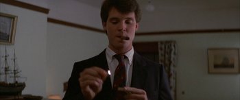 Movie still from “April Fool's Day” (1986), directed by Fred Walton – A man in a suit and tie smoking a cigarette; Close Up shot, Low angle
