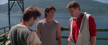 Movie still from “April Fool's Day” (1986), directed by Fred Walton – Three young men standing next to each other near a body of water; Medium shot, Over the shoulder angle