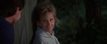 Movie still from “April Fool's Day” (1986), directed by Fred Walton – A young woman smiles for the camera while leaning against a wall; Close Up shot, Over the shoulder angle