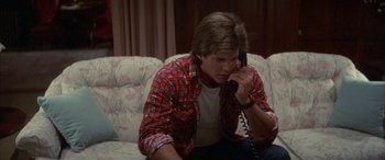 Movie still from “April Fool's Day” (1986), directed by Fred Walton – A man sitting on a couch talking on a phone; Medium shot, Low angle