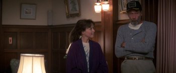 Movie still from “April Fool's Day” (1986), directed by Fred Walton – A young girl wearing a purple robe in front of a wooden wall; Medium shot, Over the shoulder angle