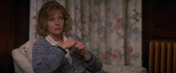 Movie still from “April Fool's Day” (1986), directed by Fred Walton – A woman sitting on a couch in front of a floral curtain; Close Up shot, Over the shoulder angle