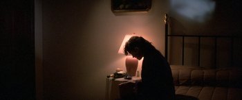 Movie still from “April Fool's Day” (1986), directed by Fred Walton – A woman sitting at a table in front of a lamp; Medium shot, High angle