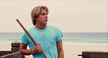 Movie still from “Aquamarine” (2006), directed by Elizabeth Allen Rosenbaum – A man holding a wooden stick on the beach; Medium shot, Low angle