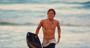 Movie still from “Aquamarine” (2006), directed by Elizabeth Allen Rosenbaum – A man holding a surfboard while standing in the ocean; Medium shot, Low angle