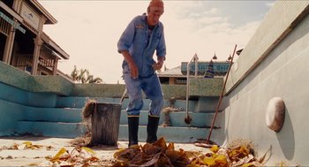 Movie still from “Aquamarine” (2006), directed by Elizabeth Allen Rosenbaum – An old man in a blue suit is raking leaves on the ground; Wide shot, Low angle