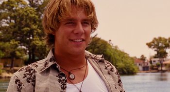 Movie still from “Aquamarine” (2006), directed by Elizabeth Allen Rosenbaum – A man with blonde hair and a white t - shirt is smiling; Close Up shot, Over the shoulder angle