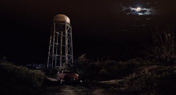 Movie still from “Aquamarine” (2006), directed by Elizabeth Allen Rosenbaum – An old car parked in front of a water tower at night; Extreme Wide shot, High angle